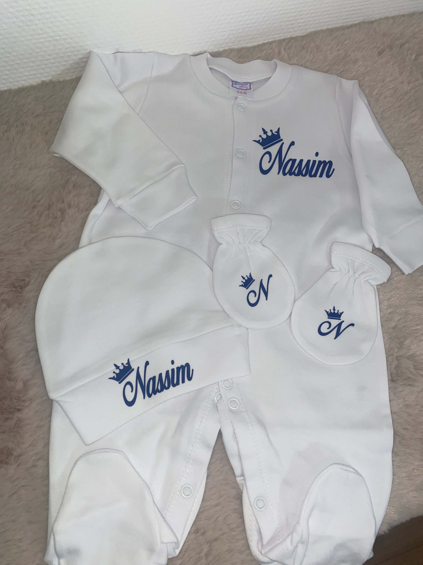 Pyjamas bébé personnalisés blancs avec des gants et un bonnet assortis, nom Nassim brodé en bleu.