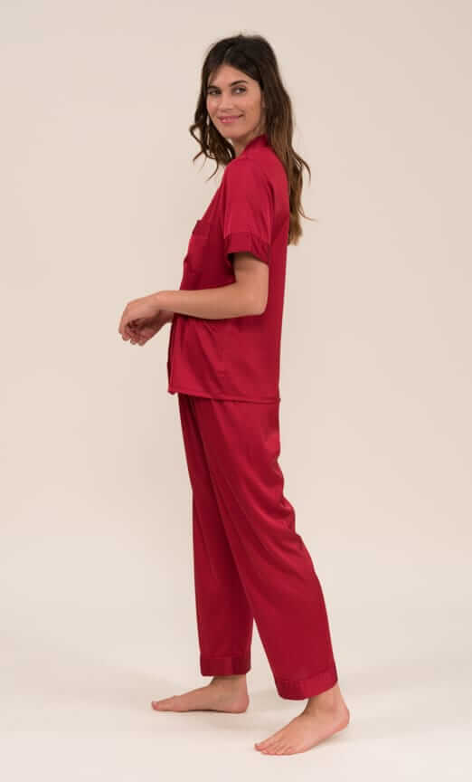 Femme portant un ensemble de pyjama en satin bordeaux avec manches courtes, composé de 97% polyester et 3% élasthanne.