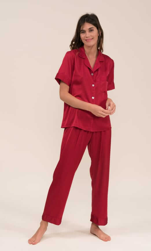 Woman wearing bordeaux short sleeve satin pajama set with matching pants, made of 97% polyester and 3% elastane, standing barefoot.