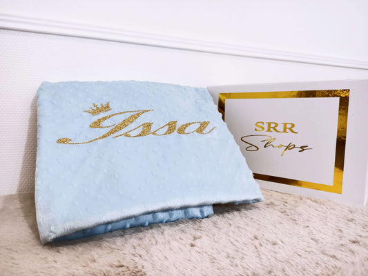 Personalized blue baby blanket with name 'Issa' in gold script next to SRR Shops sign.